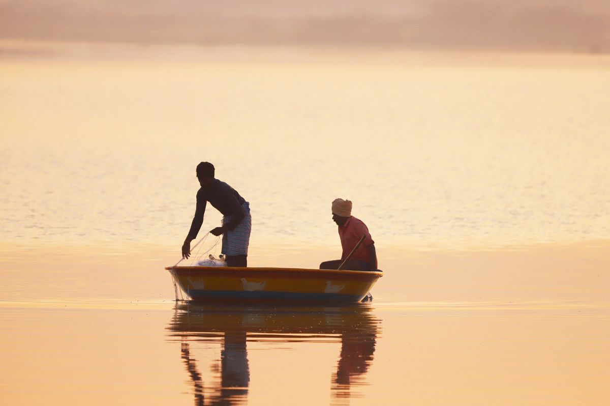 Dois pescadores em um barco ao amanhecer, água calma e luz dourada
